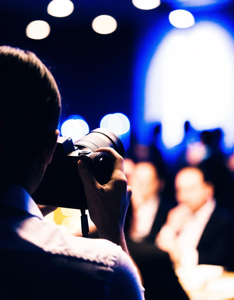 Escena ilustrativa: una persona de espaldas encuadra con su camara entre luces desenfocadas de salon.