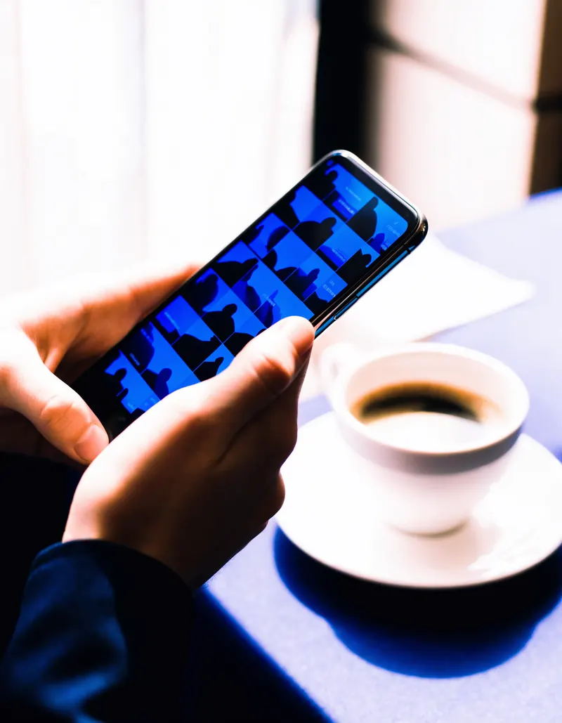 Escena ilustrativa: una mano recorre una galeria de fotografias en la pantalla de un telefono, junto a una taza de cafe.